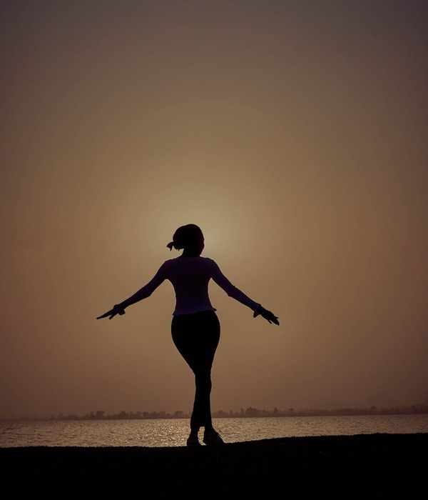 Woman holding a graceful balancing yoga pose in a dark room.